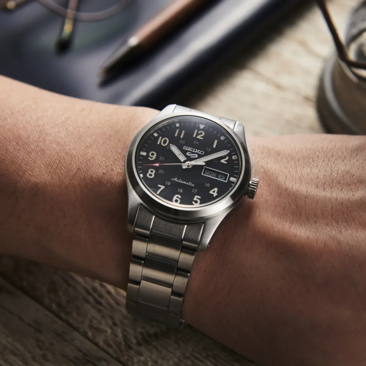 Gros plan de la montre portée au poignet, angle latéral, fond flou sur surface en bois.