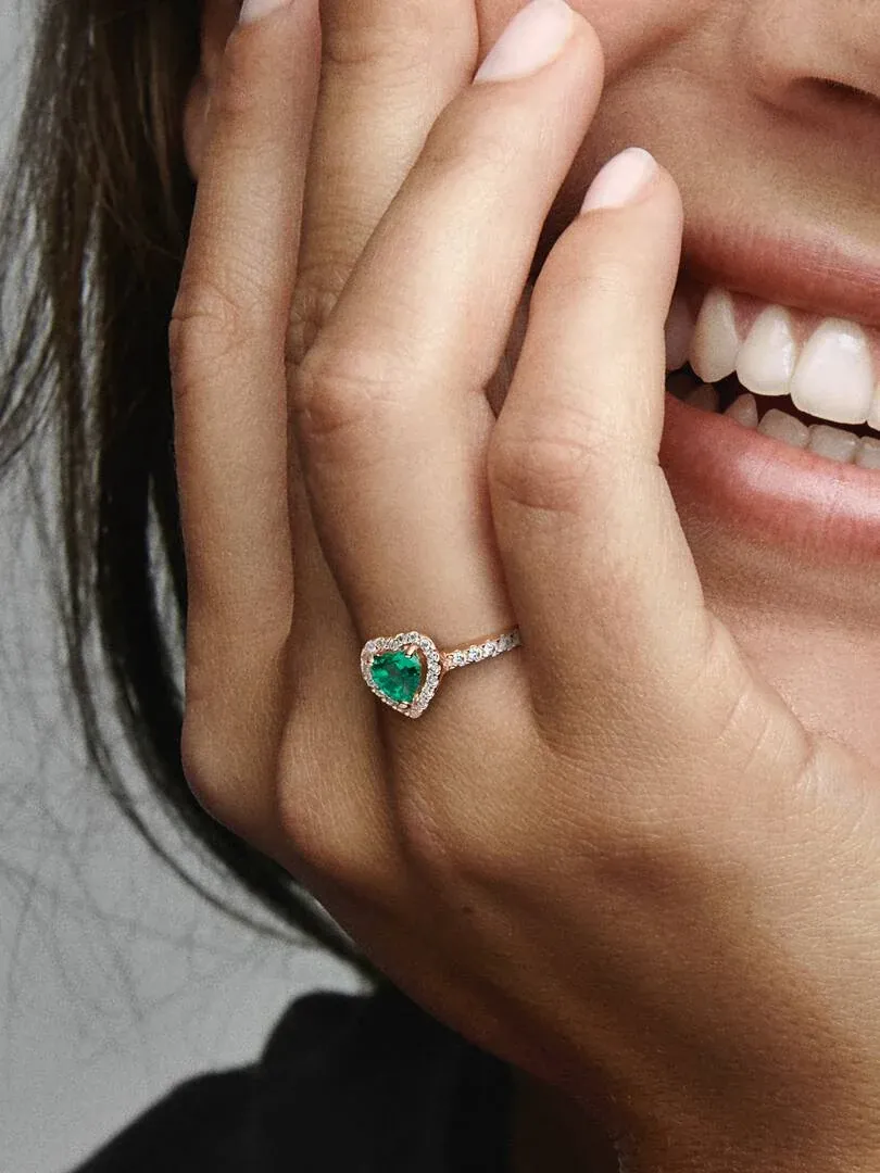 Nahaufnahme des Rings mit grünem Herz am Finger, neben dem Gesicht eines lächelnden Models.