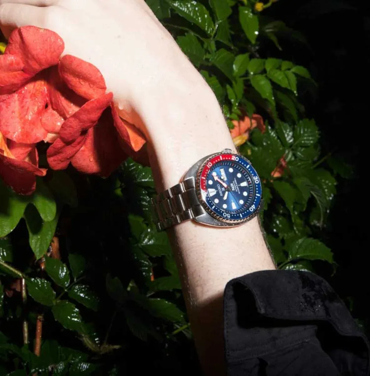 Montre au poignet sur fond de feuillage vert et fleur rouge, avec effet de peau mouillée.