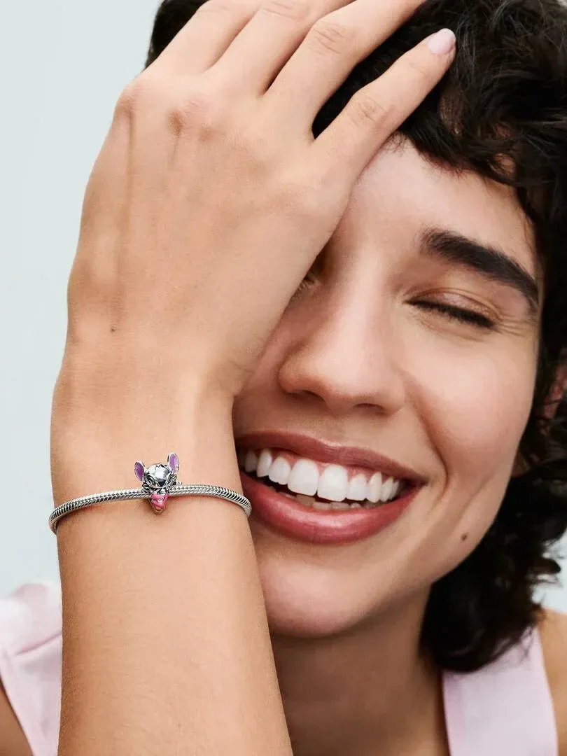 Close-up van de Stitch charm aan een armband, model lachend met de hand op het voorhoofd.