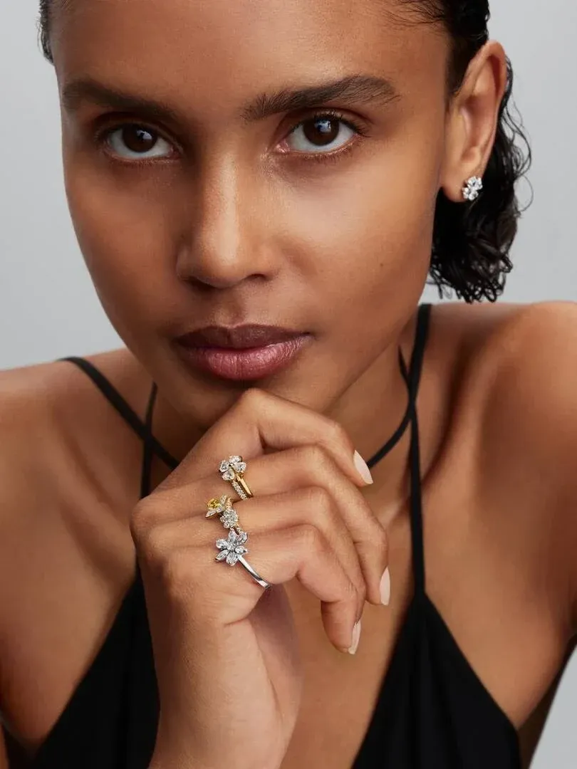 Close-up of a hand resting on the chin, showcasing the floral cubic zirconia ring against a neutral background.