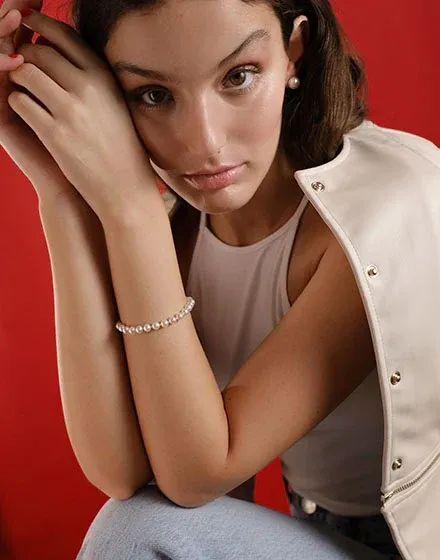 Close-up of the pearl bracelet on a wrist, model against a vibrant red background, front view.