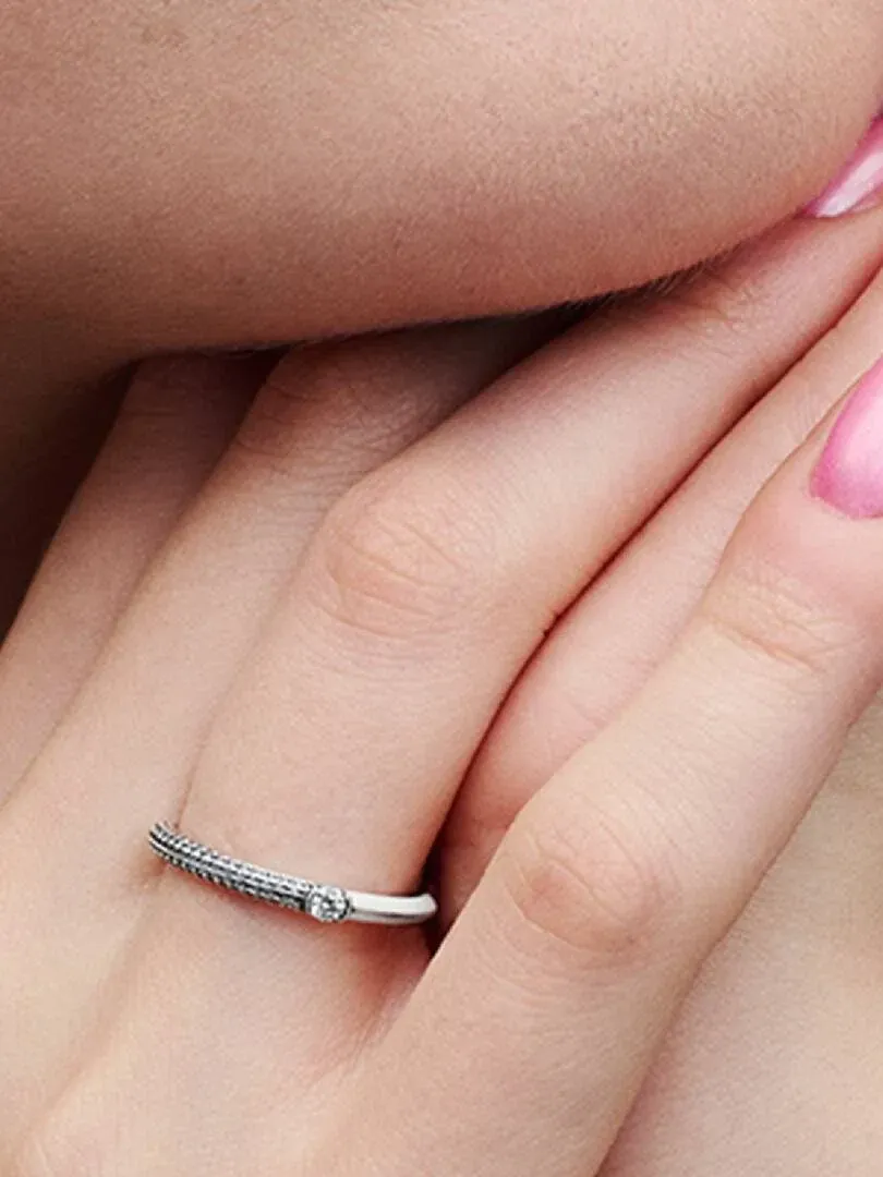 Gros plan de profil de la bague portée sur un doigt, ongles roses, fond flou.