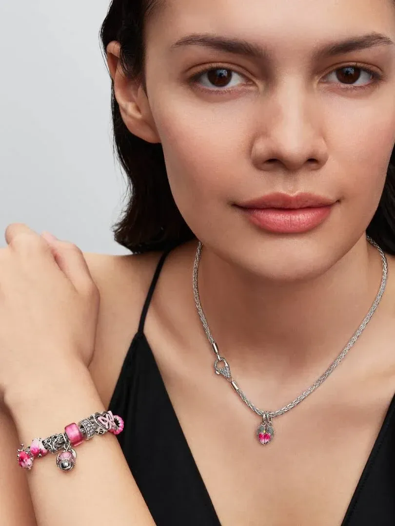 Model wearing a silver necklace and charm bracelet, medium shot against a neutral gray background.