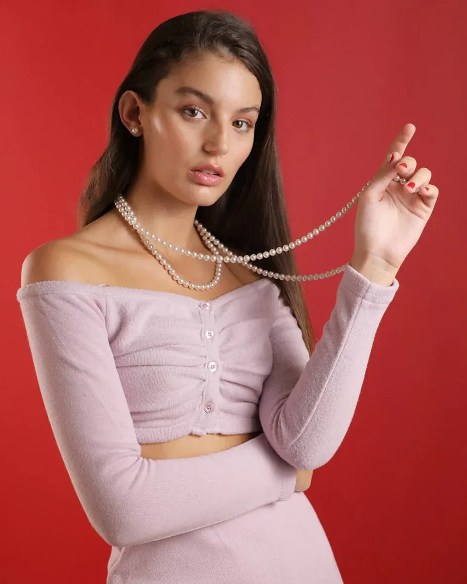 Gros plan d'un collier de perles blanches sur le cou et les épaules d'un modèle, fond rouge uni.