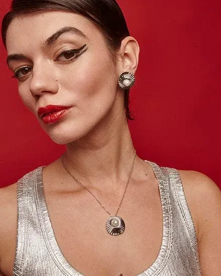 Nahaufnahme eines Models mit Perlenhalskette und Ohrringen vor lebhaft rotem Hintergrund, Frontalansicht.