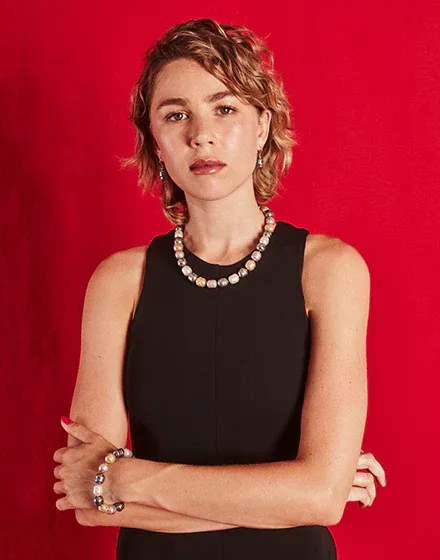 Modelo con collar de perlas barrocas y pulsera a juego, fondo rojo vibrante, plano medio frontal.