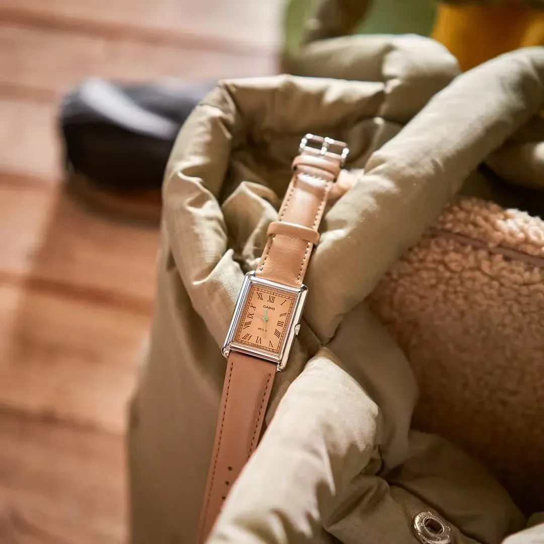 Reloj colocado sobre telas texturizadas en tonos verde oliva y beige, fondo de madera desenfocado.