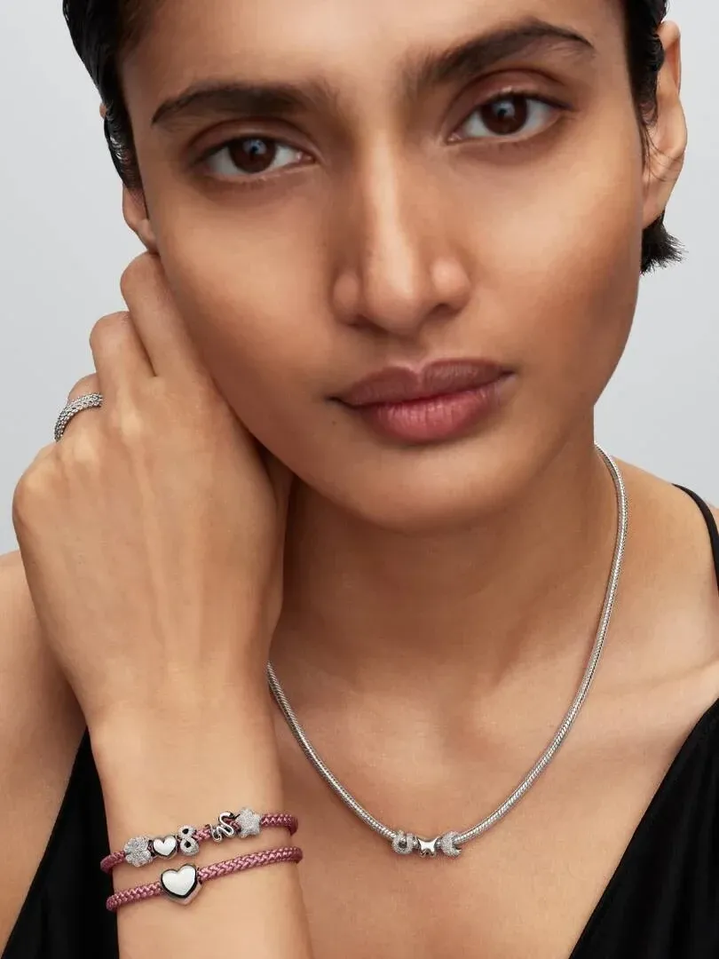 Modèle portant un collier en argent avec charms, bracelet rose avec pendentifs cœur et papillon, fond neutre.