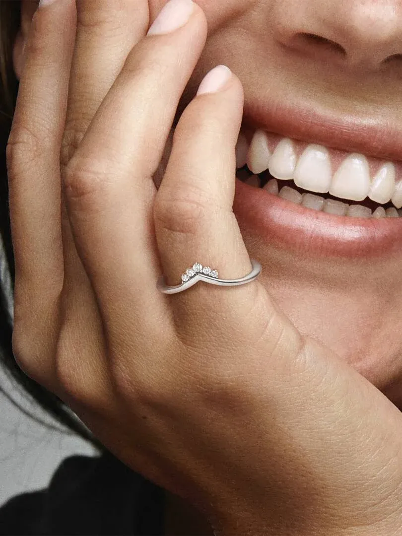 Gros plan de la bague en argent avec zircons sur un doigt, près d'un sourire, fond flou.