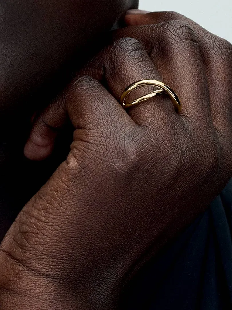 Gros plan de la bague dorée organique portée sur un doigt, vue de profil sur peau foncée.