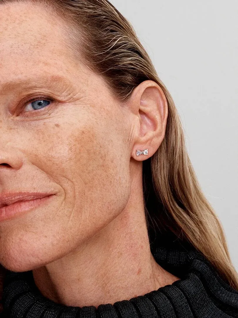 Gros plan d'une boucle d'oreille nœud étincelante portée sur le lobe de l'oreille, vue de profil.