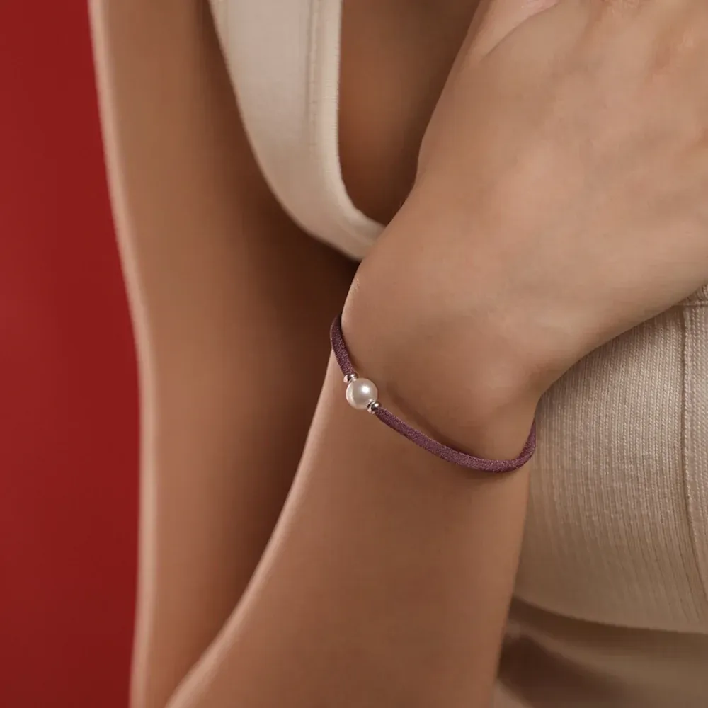 Primer plano de la pulsera magenta con perla blanca en la muñeca, toma lateral sobre fondo rojo.
