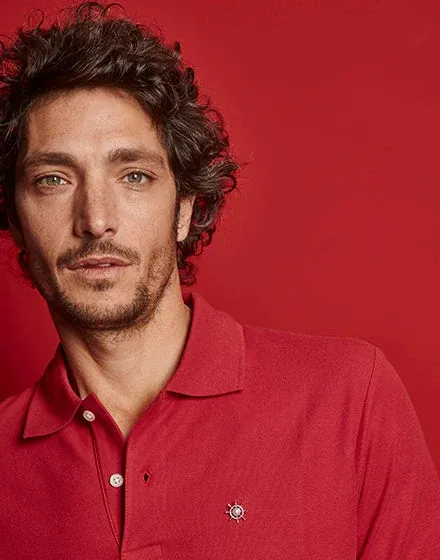 Primer plano de un hombre con polo rojo, mostrando el pin náutico sujeto en la zona del pecho.