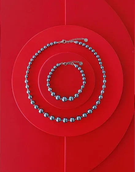 Collar y pulsera de perlas grises dispuestos en círculos concéntricos sobre fondo rojo vibrante.
