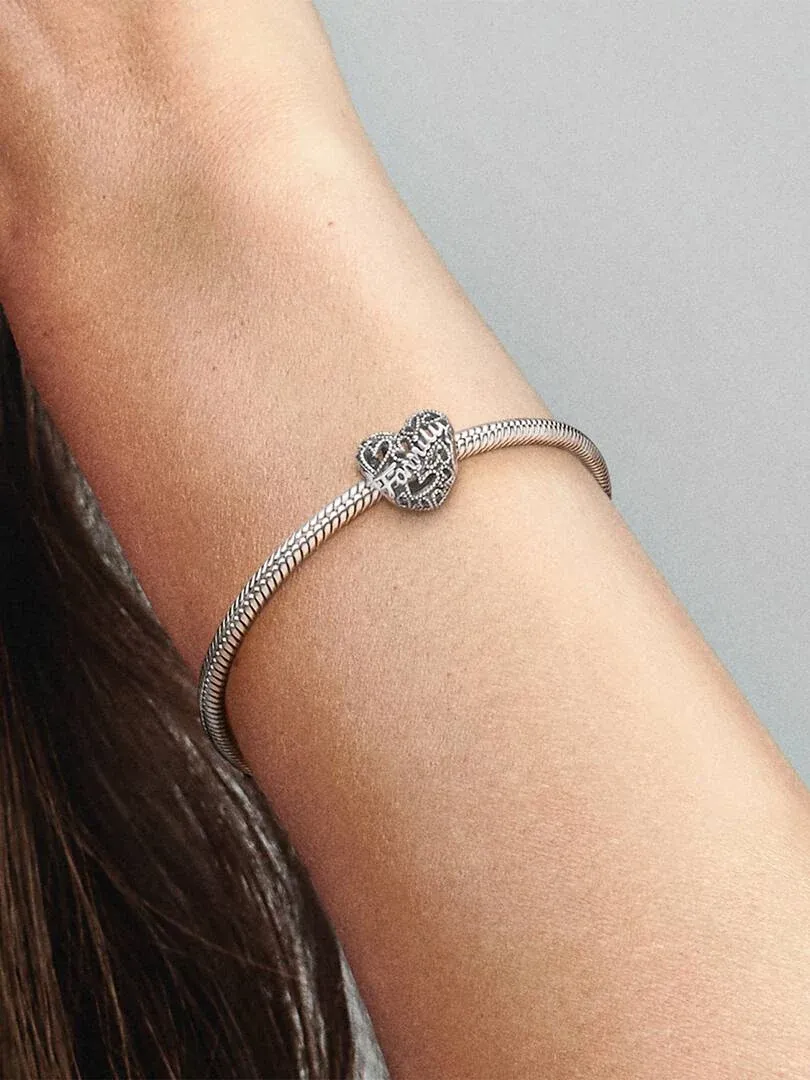 Close-up van de armband met hart charm om een pols, zijaanzicht tegen een neutrale achtergrond.