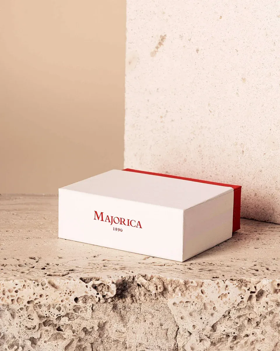 Caja blanca de joyería con logotipo rojo sobre superficie de piedra texturizada, ángulo lateral.