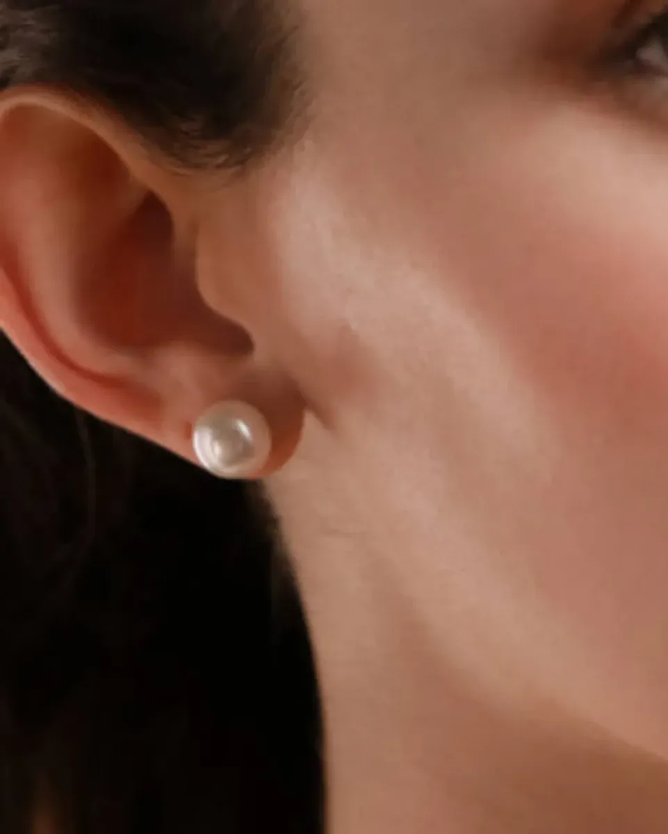 Pendiente de perla blanca puesto en el lóbulo de la oreja, primer plano lateral.