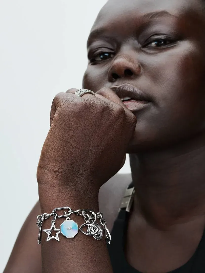 Close-up of the link bracelet with charms on a wrist, side view against a neutral background.