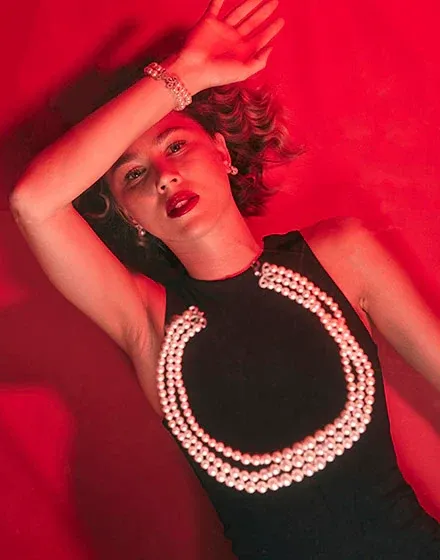 Modelo con collar de doble hilera de perlas y pulsera a juego, sobre fondo rojo vibrante, toma cenital.
