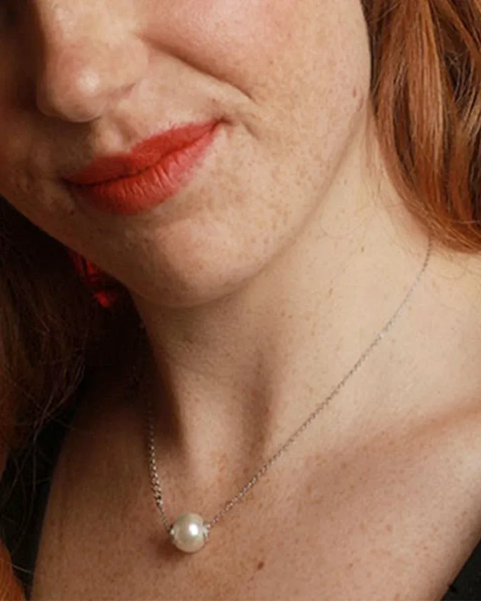 Primer plano del collar con perla blanca sobre el cuello de una modelo, toma frontal con fondo desenfocado.
