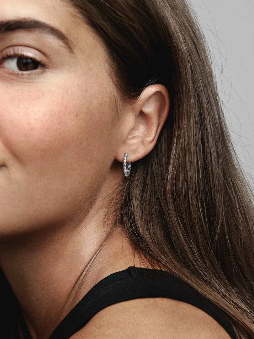 Gros plan latéral d'une boucle d'oreille créole en argent portée sur l'oreille, modèle aux cheveux châtains.