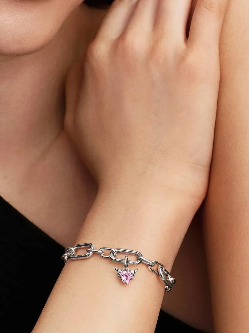 Gros plan du poignet avec bracelet à maillons et pendentif cœur rose, vue de profil.
