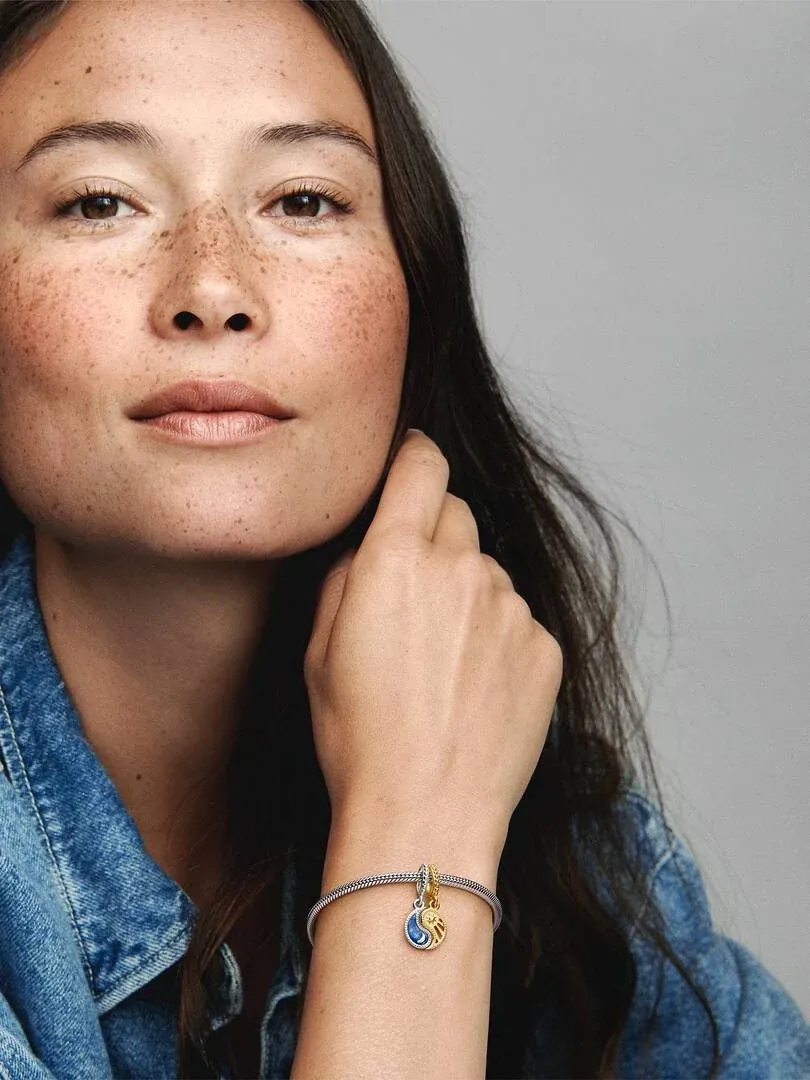 Close-up of the wrist wearing the Sun and Moon charm, model in denim shirt against a neutral gray background.