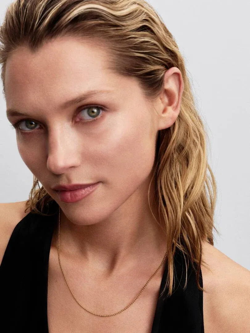 Nahaufnahme der goldenen Halskette am Hals eines Models, Frontansicht vor hellem neutralem Hintergrund.