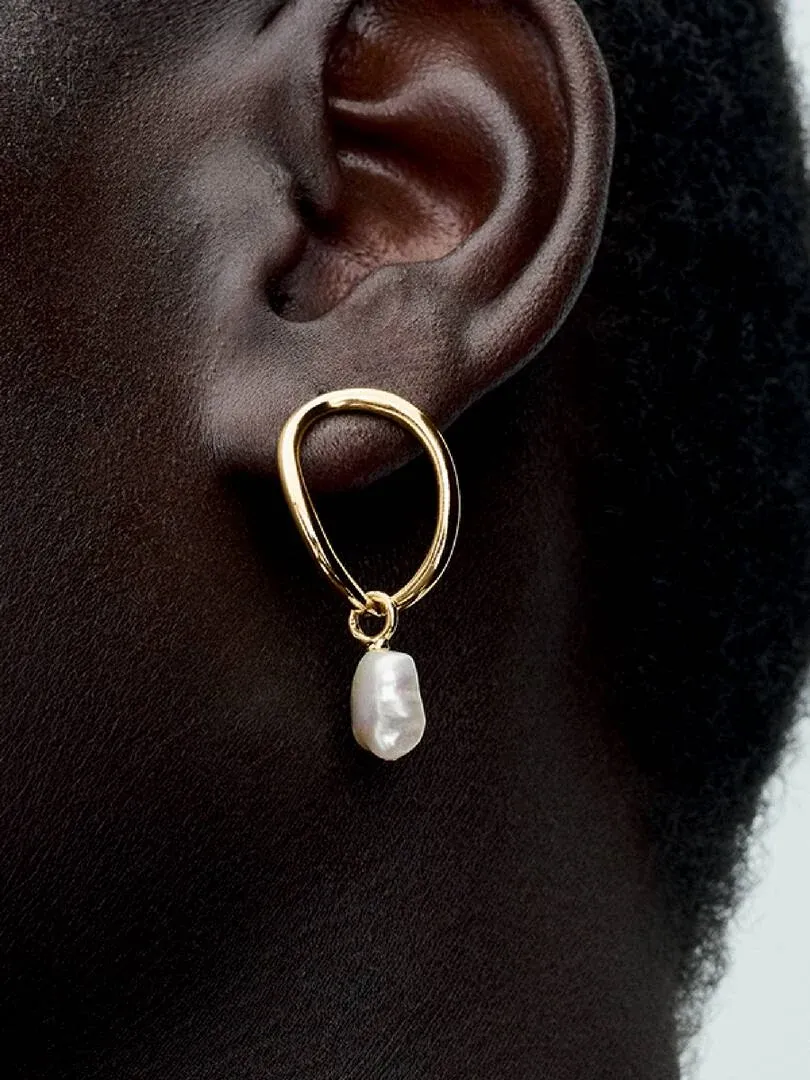 Gros plan latéral d'une boucle d'oreille perle baroque portée à l'oreille, fond sombre flou.