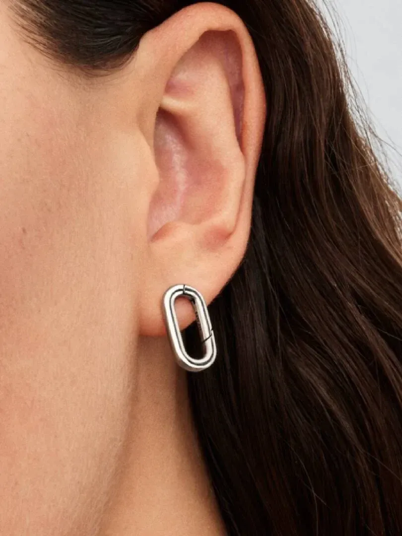 Zijaanzicht close-up van een ovale zilveren oorring gedragen aan het oor, wazige achtergrond.