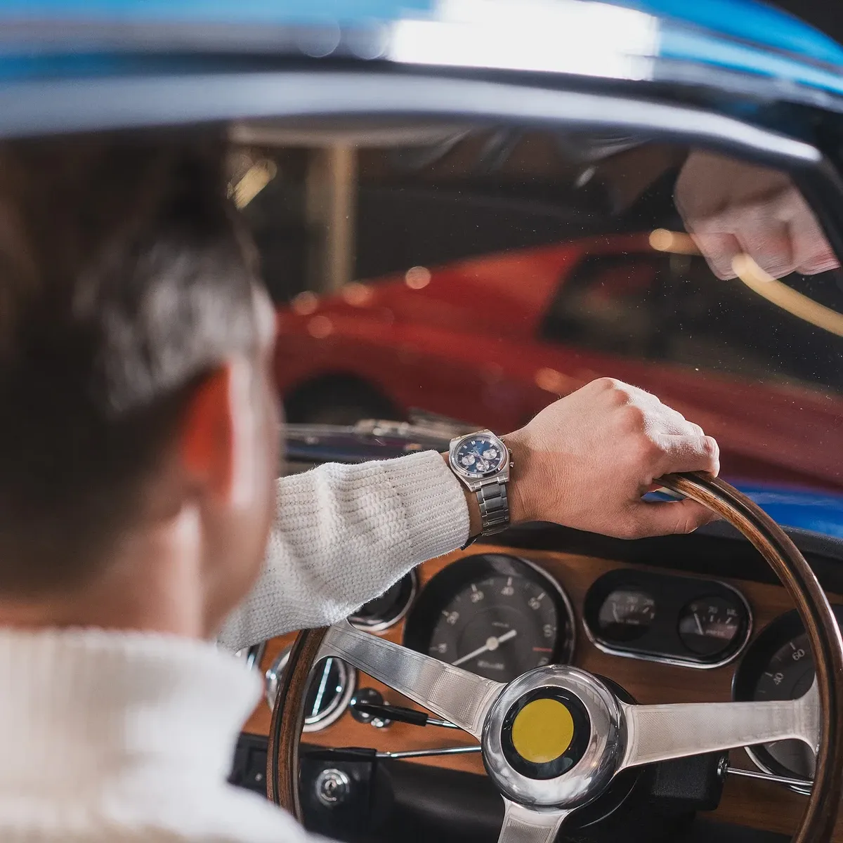 Reloj puesto en muñeca masculina sujetando el volante de madera de un coche clásico, fondo de salpicadero.