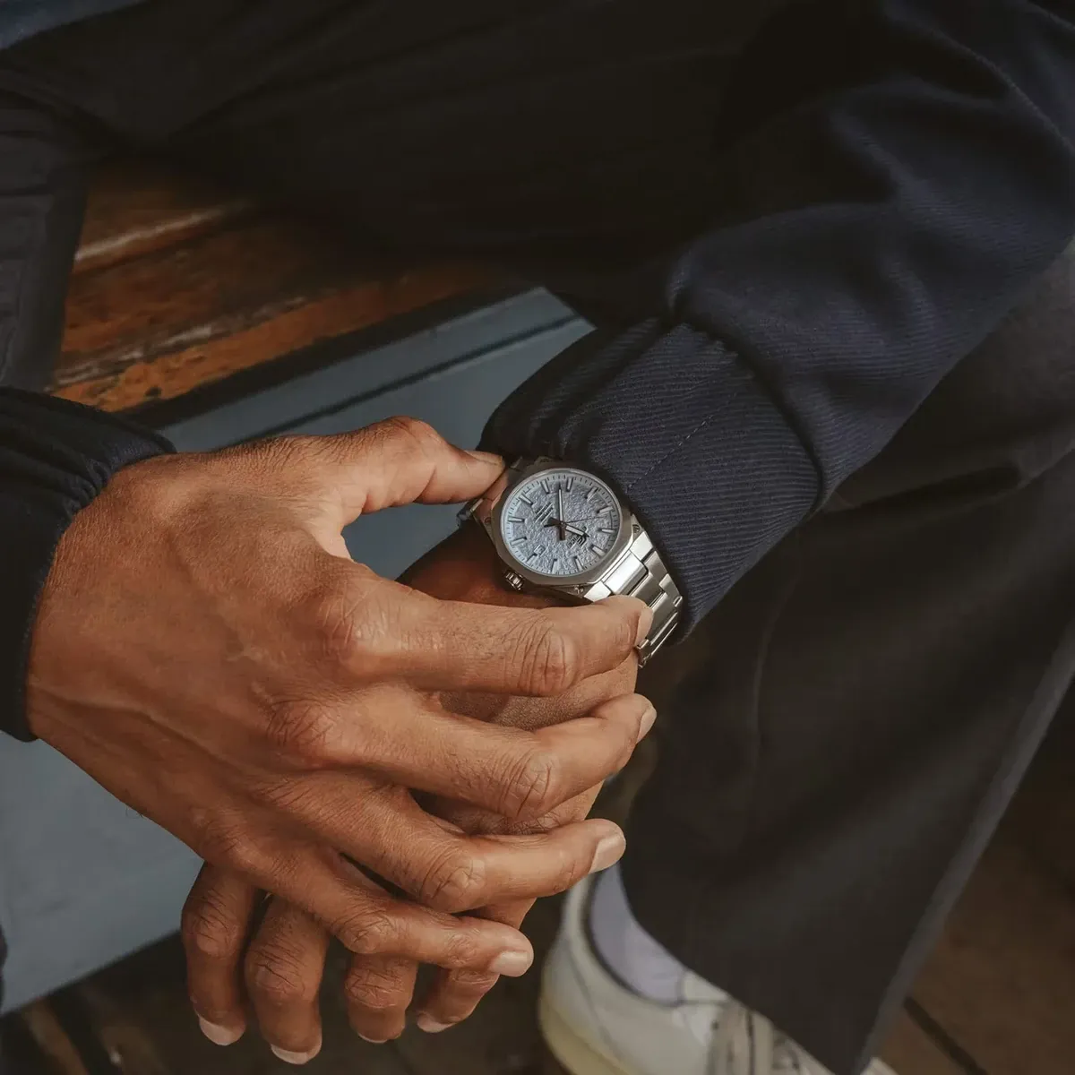 Reloj puesto en la muñeca de un modelo con traje azul marino, primer plano de las manos entrelazadas.