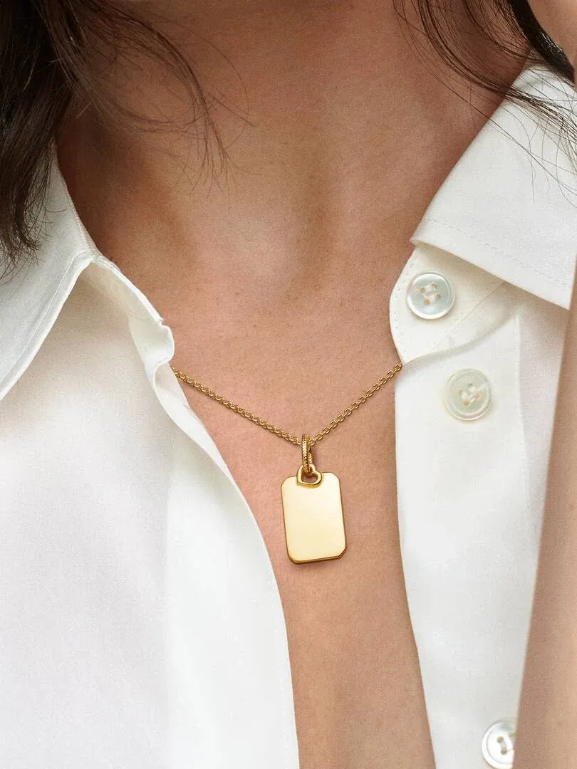 Nahaufnahme des goldenen rechteckigen Anhängers auf einem weißen Hemd, Frontansicht am Ausschnitt.