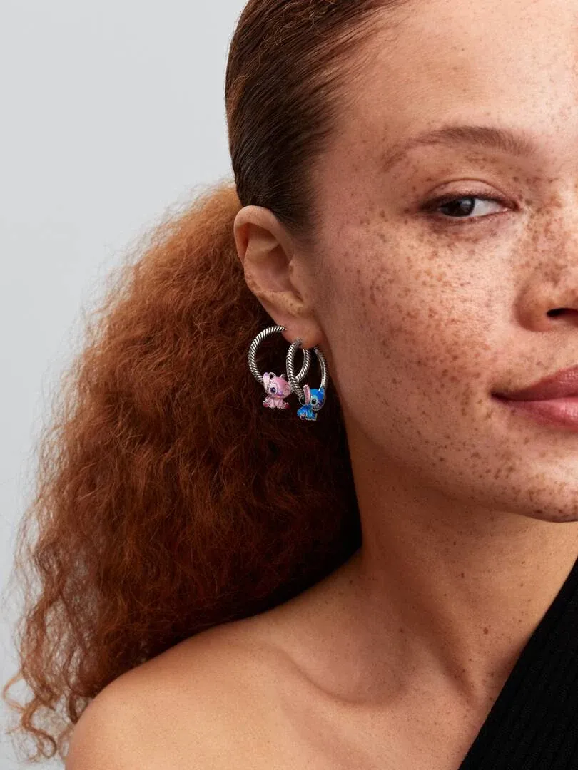 Gros plan latéral d'une boucle d'oreille créole avec pendentifs personnages rose et bleu, portée par un modèle.