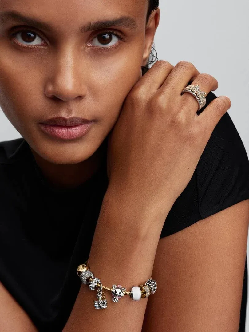 Close-up of a model wearing a ring and charm bracelet, side view against a neutral background.