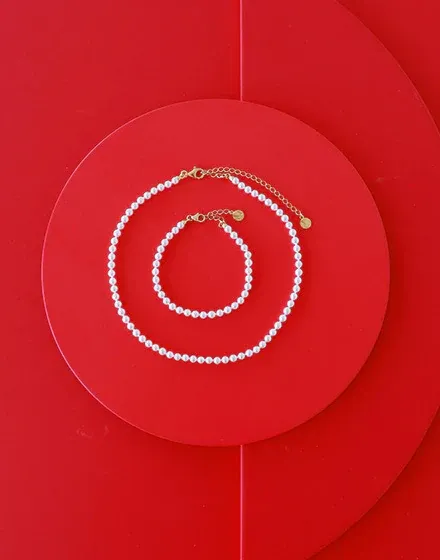 Collar y pulsera de perlas dispuestos en círculos concéntricos sobre fondo rojo vibrante.