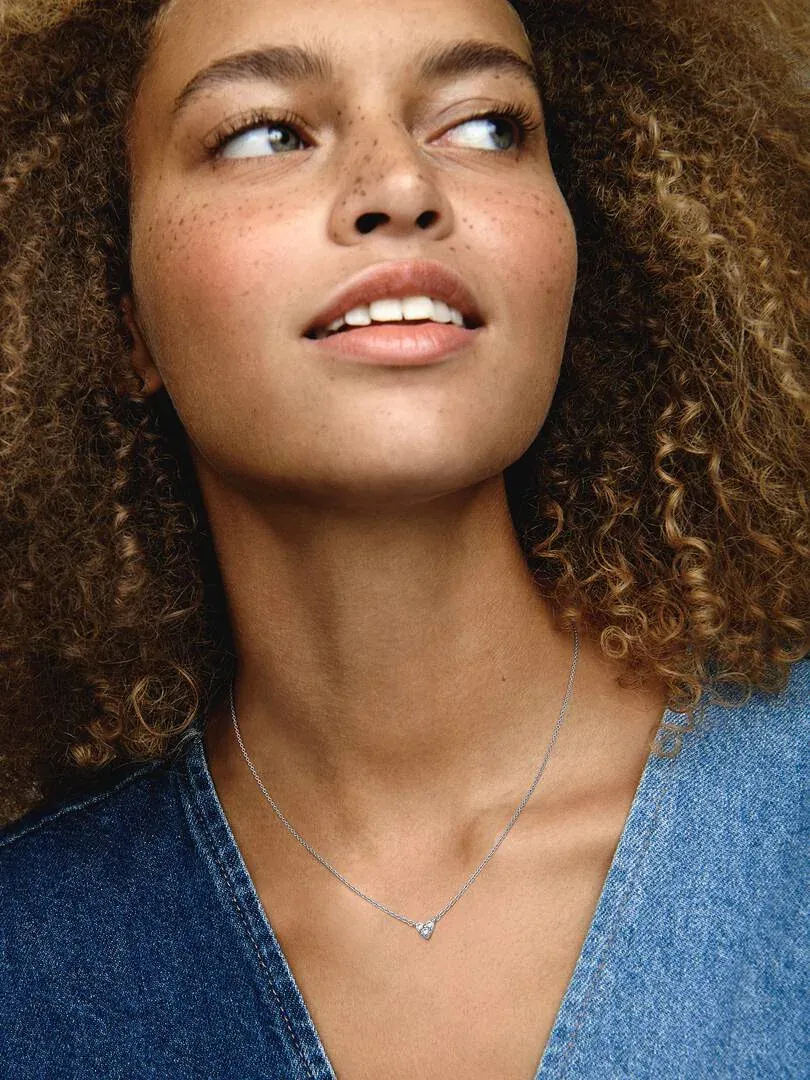 Close-up van de zilveren ketting met hart hanger om de hals van een model, wazige achtergrond.