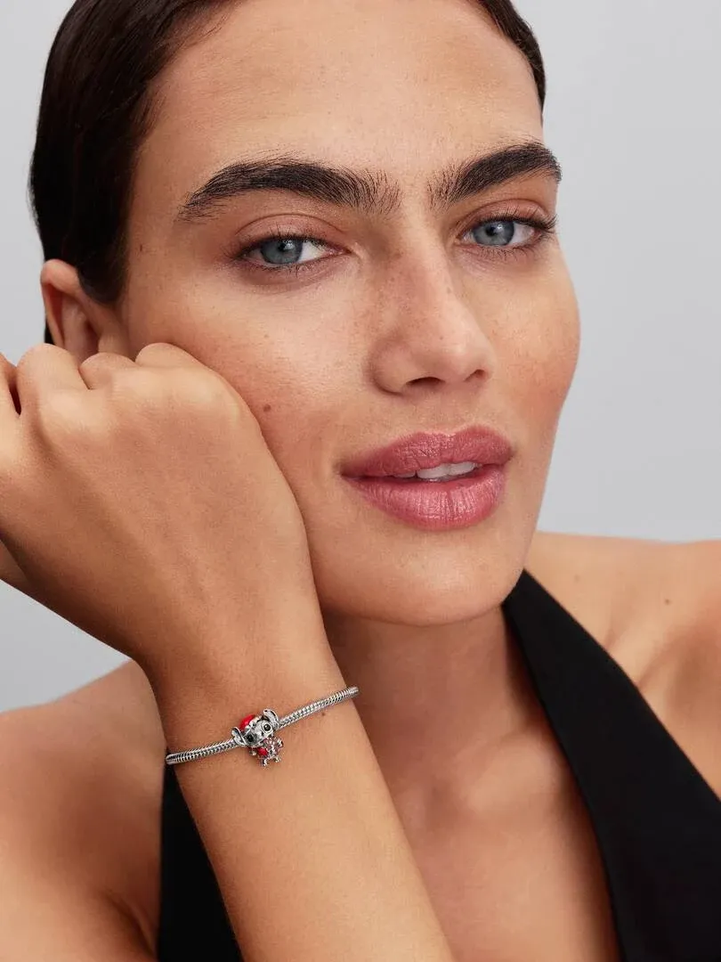 Nahaufnahme des Stitch-Charms an einem Armband, gehalten von der Hand eines Models vor neutralem Hintergrund.