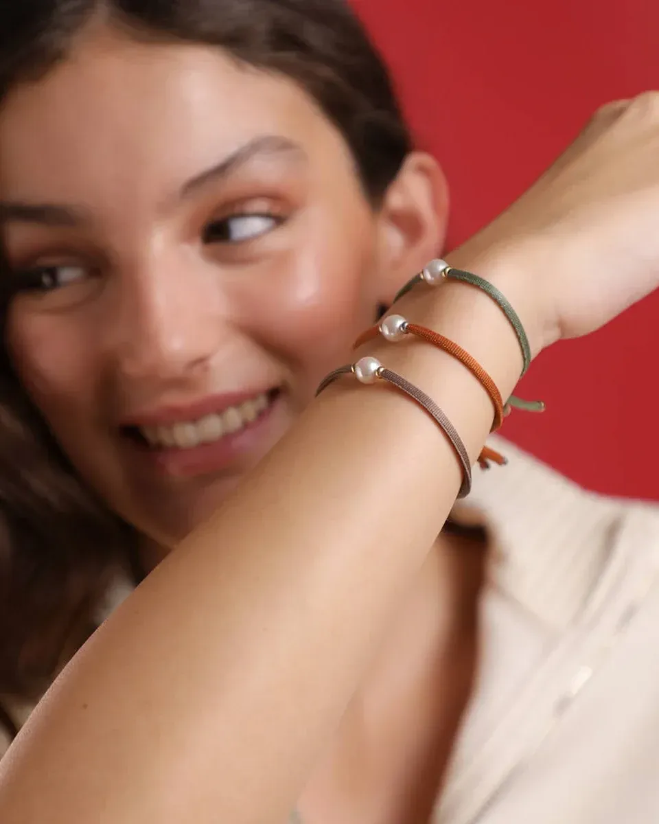 Primer plano de tres pulseras elásticas con perlas en la muñeca, toma lateral sobre fondo rojo vibrante.