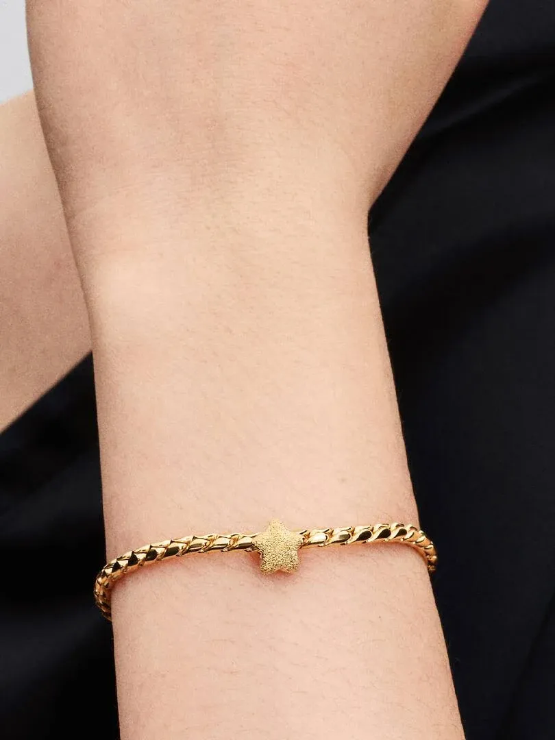 Close-up of the gold star charm bracelet worn on a wrist, side view against a dark background.