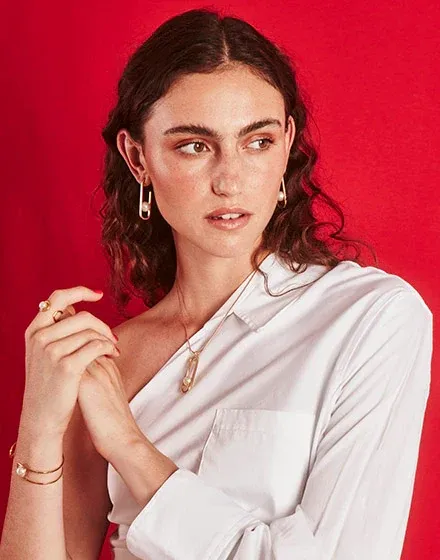 Model wearing pearl bracelet, necklace, and earrings against a vibrant red background, medium shot.