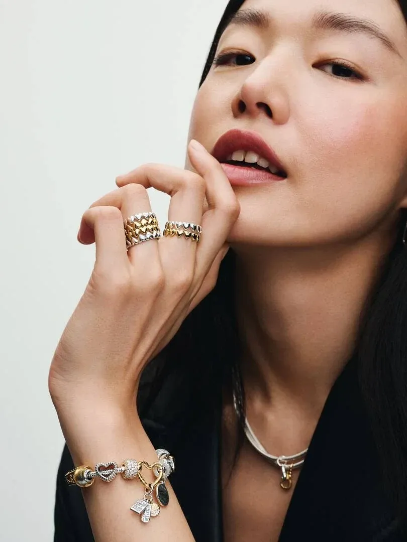 Close-up van model met charm armband en ringen aan de vingers, zijaanzicht tegen lichte achtergrond.