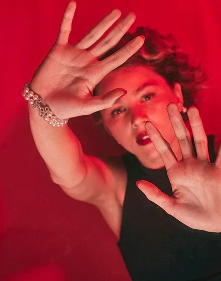 Close-up of the bracelet on the wrist, hands raised in front of a model against a vibrant red background.