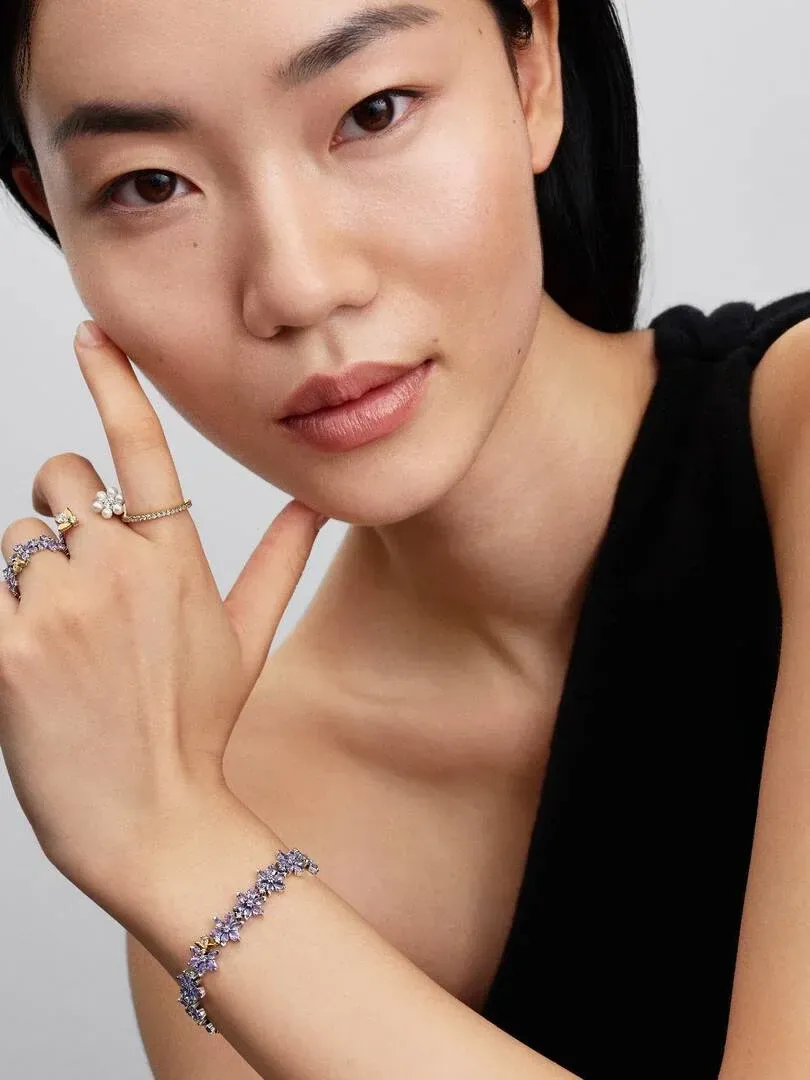 Close-up of wrist and hand wearing purple flower bracelet and rings, on model in black top.