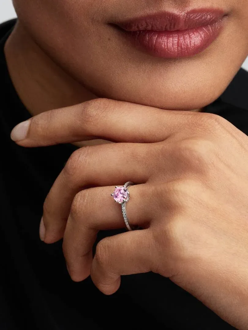 Nahaufnahme des Rings mit fuchsiafarbener Zirkonia an einem Finger, Seitenansicht vor dunklem Hintergrund.