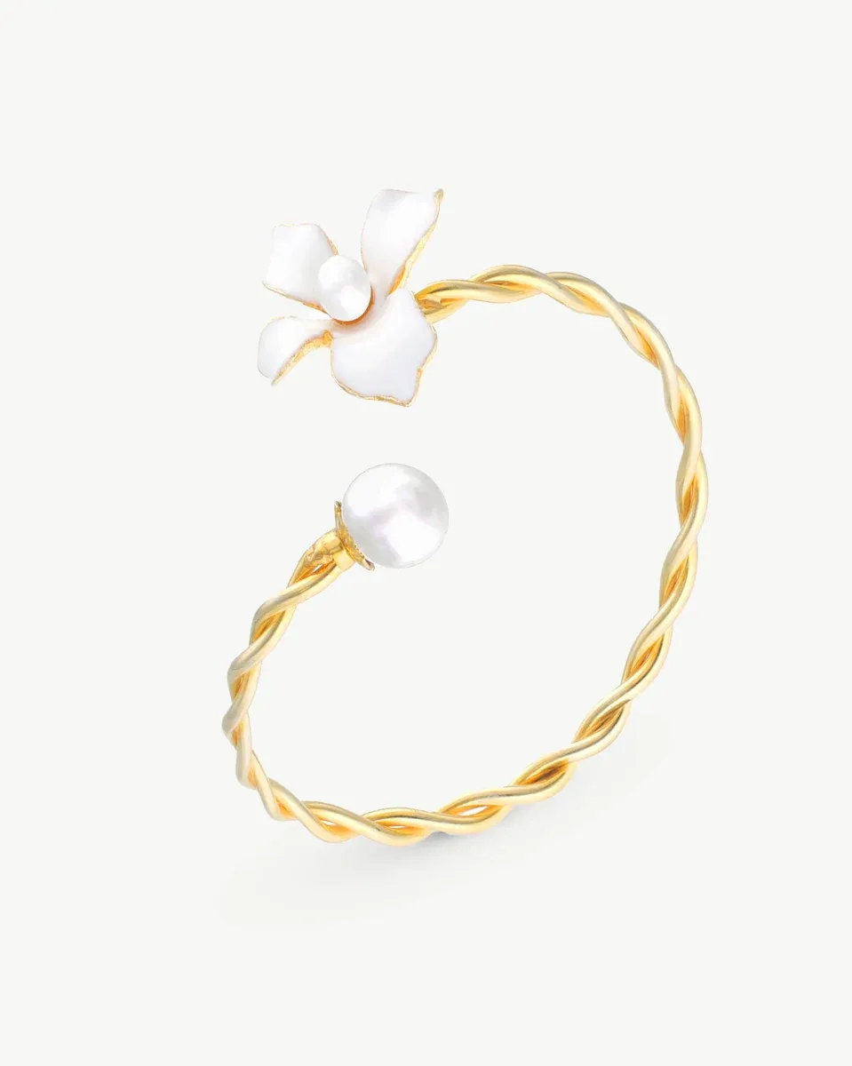 Brazalete de oro con diseño trenzado, flor blanca esmaltada y perla, vista lateral sobre fondo blanco.