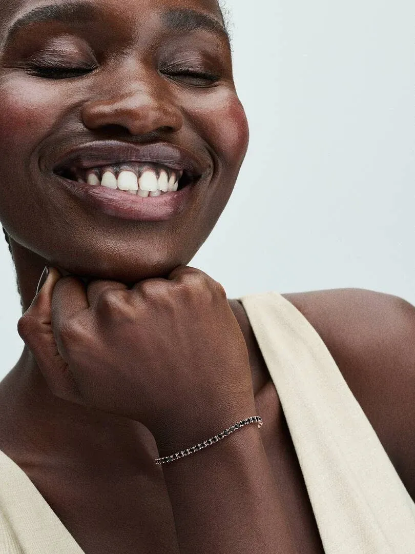 Nahaufnahme des Armbands am Handgelenk, Seitenansicht mit lächelndem Modell vor neutralem Hintergrund.