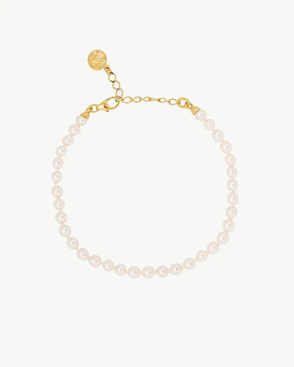 Pearl bracelet arranged in a circle on a white background, top view showing the clasp and charm.