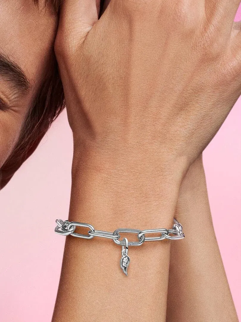 Close-up of silver link bracelet with angel wing charm on wrist, pink background.